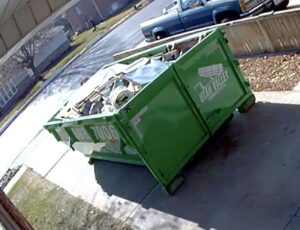 A green dumpster filled with various junk on a residential driveway by Utah Valley Dumpsters in Provo, UT.