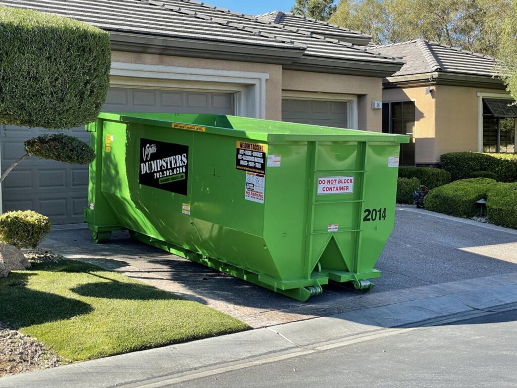 A green dumpster from Junk Control placed in a residential driveway for a junk removal project in Henderson, NV.