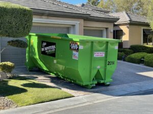 A green dumpster from Junk Control placed in a residential driveway for a junk removal project in Henderson, NV.