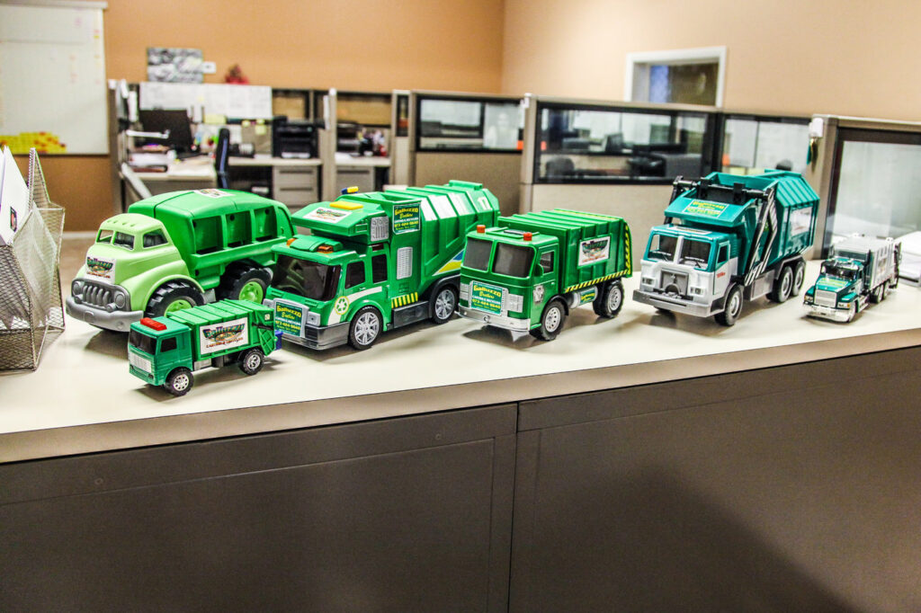 A green roll-off dumpster partially filled with various junk items on a street, provided by Galluzzo Brothers Carting in Newark, NJ.