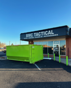A bright green dumpster from Duke City Dumpster Rentals LLC parked in front of BMC Tactical in Albuquerque, NM, ready for junk removal.