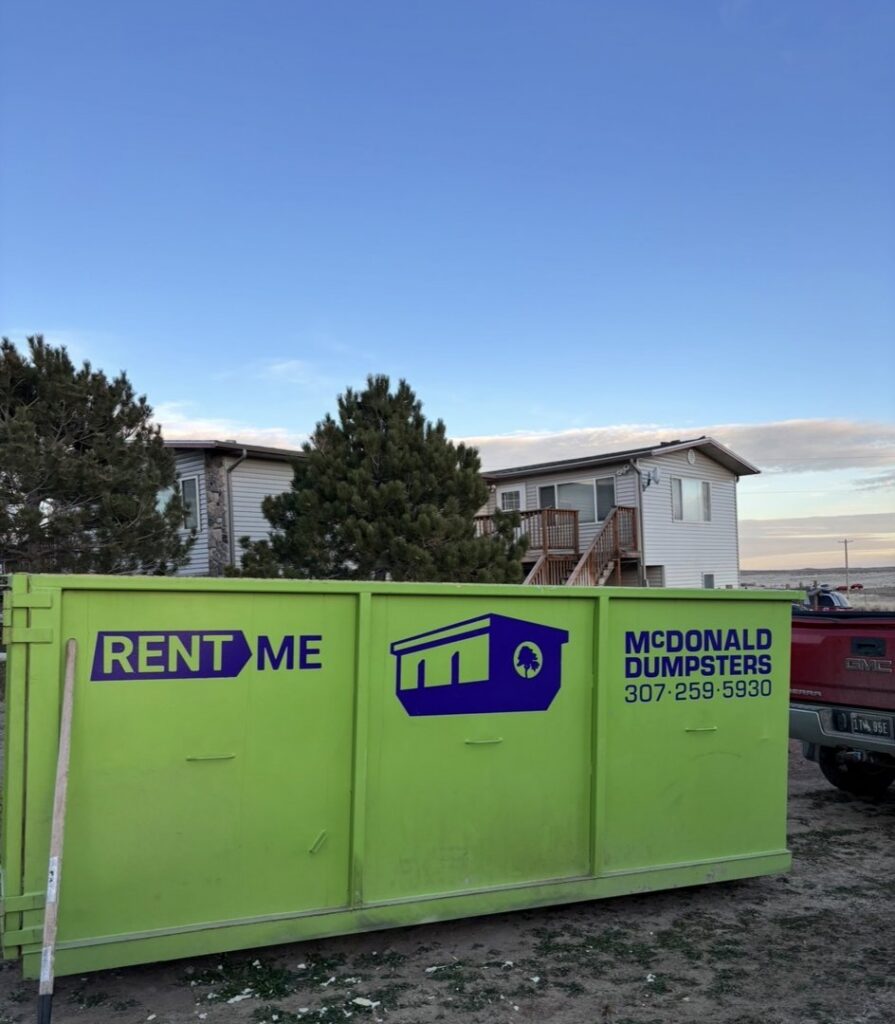 A green McDonald Dumpsters dumpster placed next to a residential building in Bar Nunn, WY.