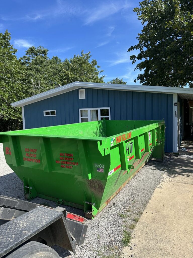 A green dumpster from American Dumpster Rentals placed in front of a residential building in Morrilton, AR.