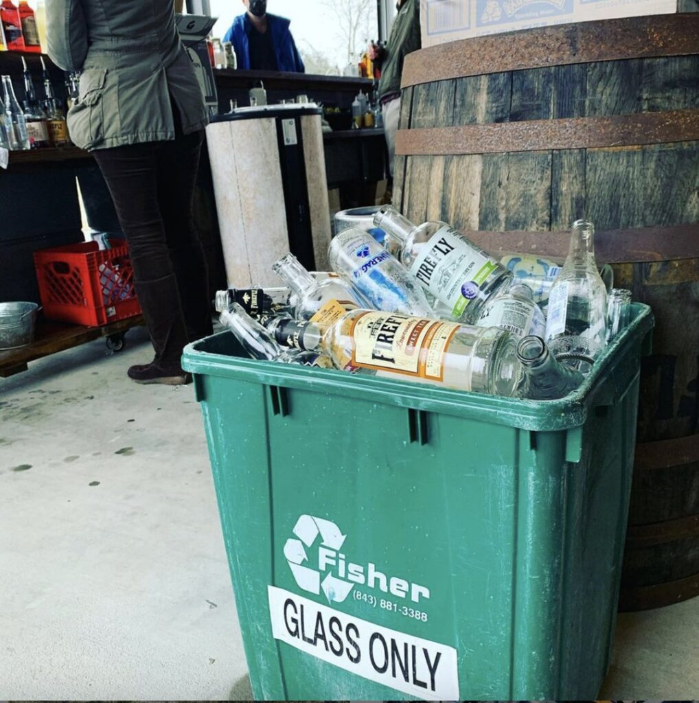 A green recycling bin from Fisher Recycling, full of glass bottles at a commercial venue in Charleston, SC.