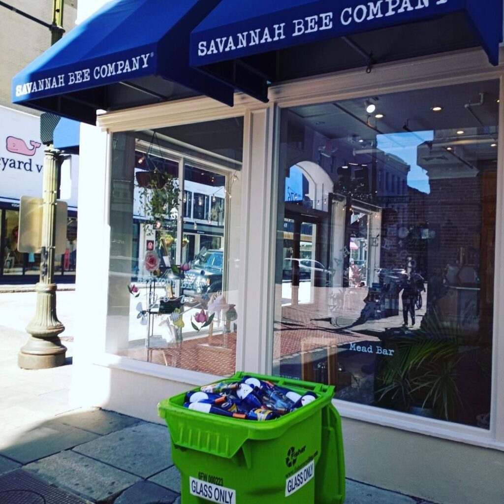 A green recycling bin overflowing with glass bottles outside a business, provided by Fisher Recycling in Charleston, SC.