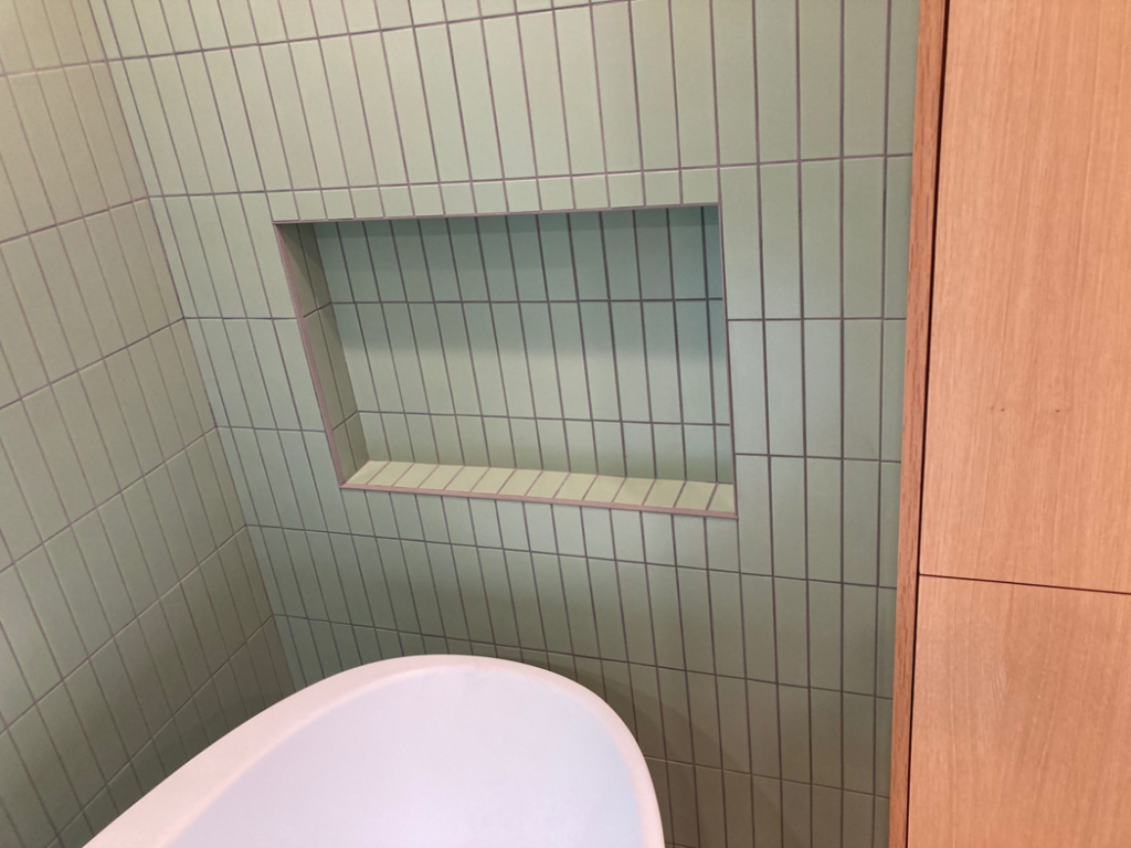 A close-up of a bathroom wall featuring green subway tiles and a built-in shower niche by Tess Tile By Design in Kansas City, MO.