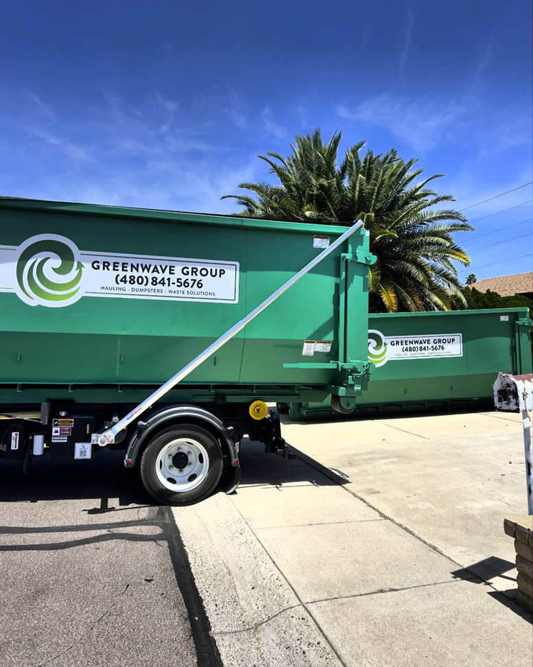 Two large green dumpsters from Greenwave Waste Solutions parked on a residential street in Glendale, AZ, for junk removal services.