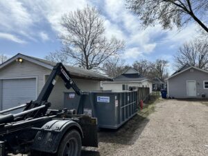 A grey dumpster from 515 Dumpsters being loaded onto a truck next to a residential garage in West Des Moines, IA.