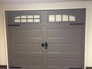 A grey garage door featuring rectangular windows and black decorative hardware, offered by Harold Carpenter Overhead Door inc in Oshkosh, WI.