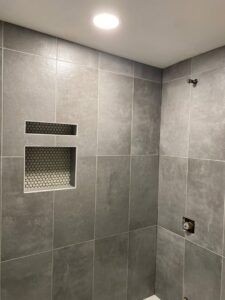 An interior view of a shower with large grey tiles and two recessed niches featuring mosaic tile backing by Tile Jawn in Philadelphia, PA.
