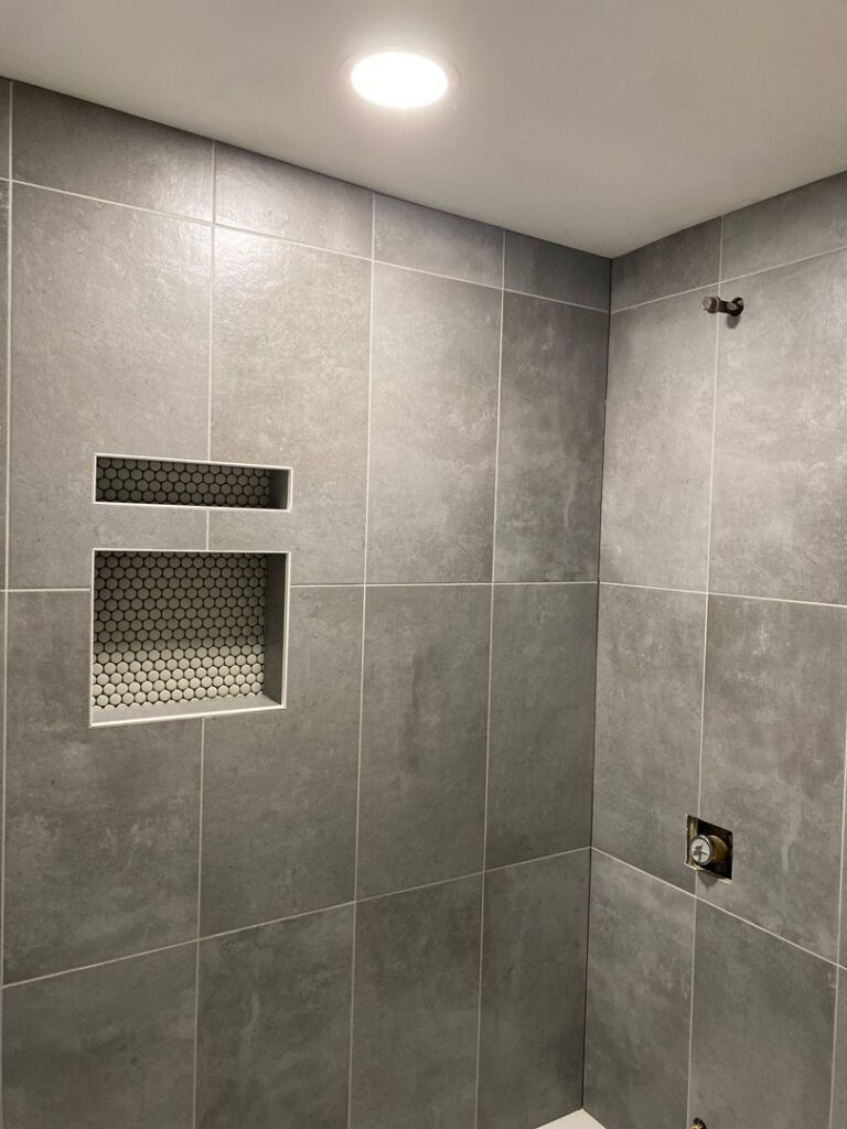 An interior view of a shower with large grey tiles and two recessed niches featuring mosaic tile backing by Tile Jawn in Philadelphia, PA.