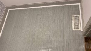 A newly installed grey tiled wall and floor with a vent by Goubar Tile And More in Raleigh, NC.