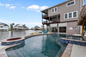 A grey waterfront home with a multi-level deck, pool, and outdoor living space by Whitley Construction Services in Houston, TX.