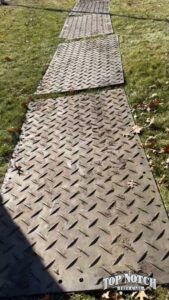 Ground protection mats with the Top Notch Tree Care logo laid out on grass in Holt, MI.