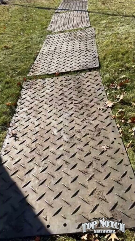 Ground protection mats with the Top Notch Tree Care logo laid out on grass in Holt, MI.