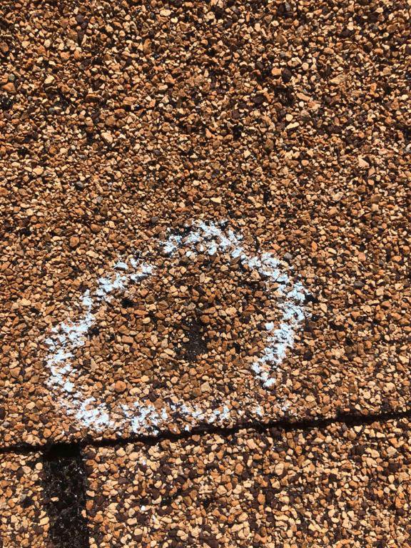 Close-up of hail damage marked on a gravel roof during an inspection by Elite Roofing Colorado Springs, CO.