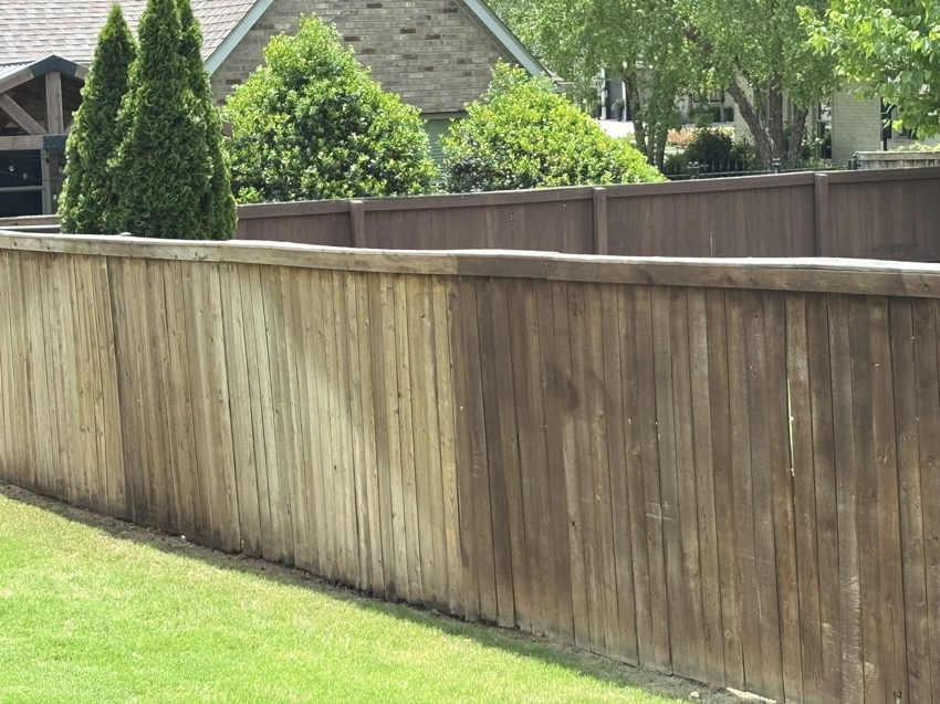 A wooden fence showing a clear before and after of pressure washing by Precise Drain & Home Services in Springdale, AR.