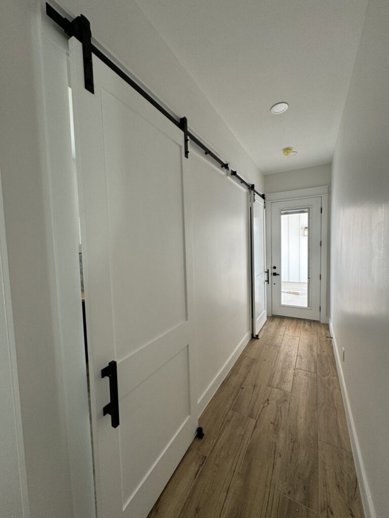 A modern hallway featuring newly installed barn doors and wood-look tile flooring, a project by Roaring Lion Renovations, LLC in Houston, TX.