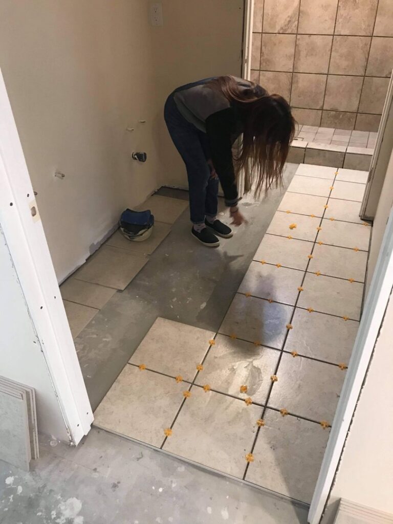 A person installing floor tiles in a hallway, using spacers for even placement, by MDJ Handyman in Salt Lake City, UT.