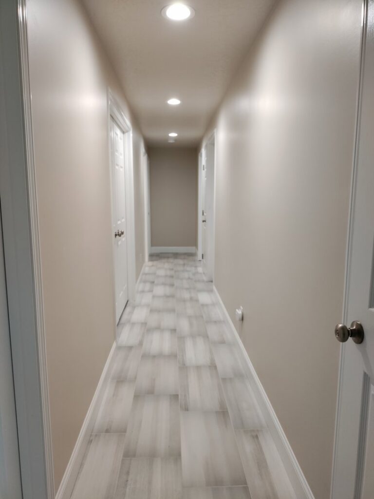 A renovated hallway featuring new wood-look tile flooring and modern recessed lighting, installed by Devco Construction LLC in West Valley City, UT
