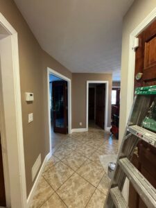A hallway with freshly painted light brown walls and a ladder, indicating an interior painting project by Quinonez Painting & Renovations LLC in Providence, RI.