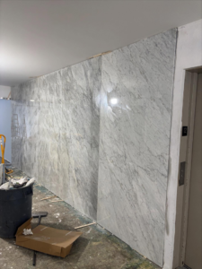 A hallway under renovation with large marble-like panels being installed by Golden Tile Construction in Yonkers, NY.