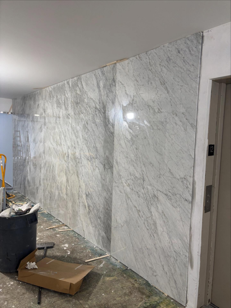 A hallway under renovation with large marble-like panels being installed by Golden Tile Construction in Yonkers, NY.