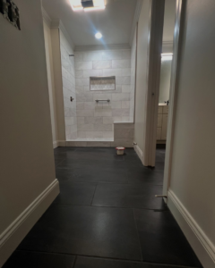 A hallway featuring newly installed dark floor tiles leading to a renovated shower, completed by TileWorks in Birmingham, AL.