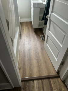 A hallway with newly installed wood-look flooring leading to a bathroom, completed by CJ Flooring LLC in Flat Rock, MI.