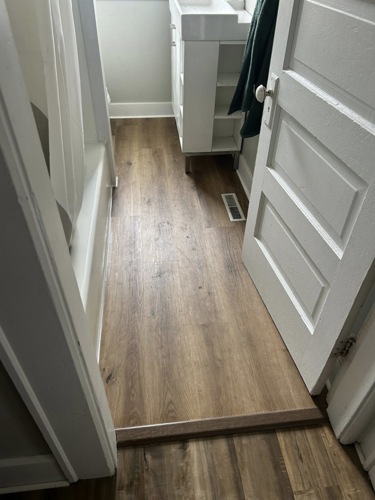 A hallway with newly installed wood-look flooring leading to a bathroom, completed by CJ Flooring LLC in Flat Rock, MI.