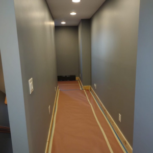 A hallway with grey painted walls and protected floors, showing a painting job in progress by SID Painting in West Hartford, CT.