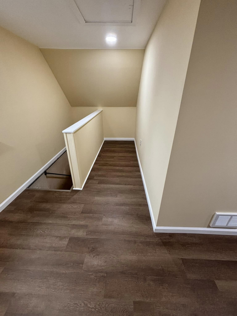 A renovated hallway with new laminate flooring, a freshly painted stair railing, and recessed lighting by T-N-T Mechanical in Westland, MI.