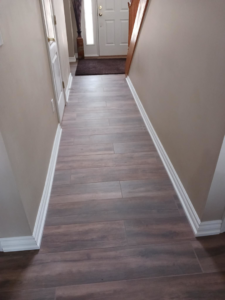 A newly installed wood-look tile floor and white baseboards in a hallway by Home Improvement Design Center in Ann Arbor, MI.