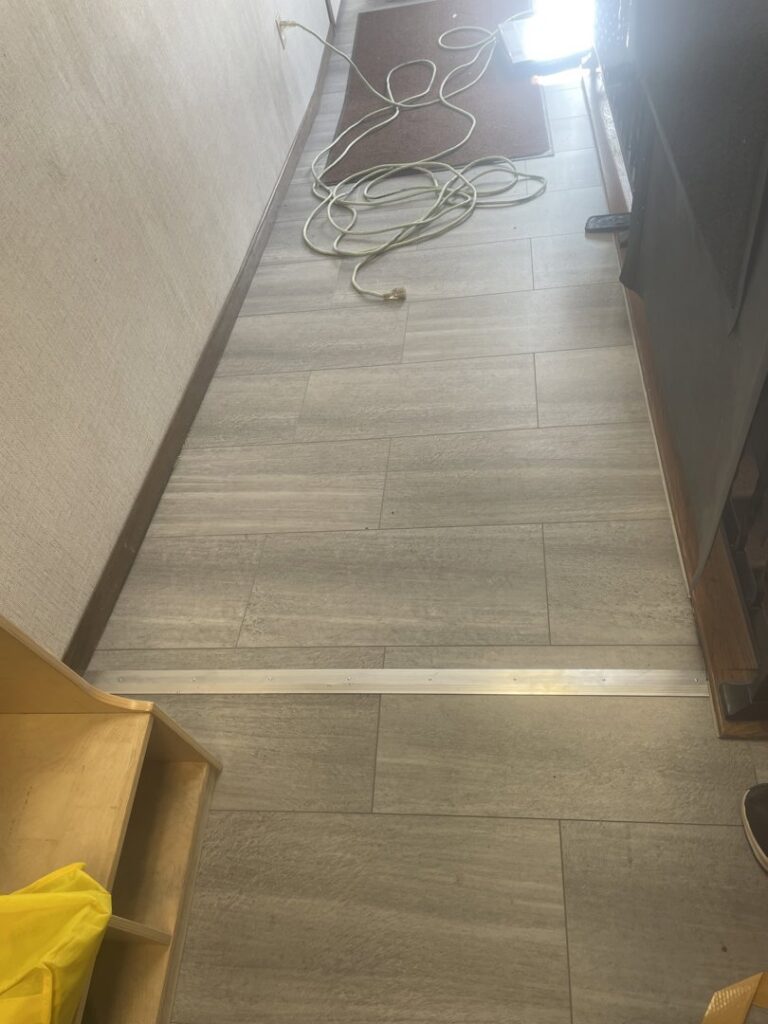 A hallway with newly installed light grey tile flooring, showcasing a completed project by Knutson's Property Maintenance Llc in Williston, ND.