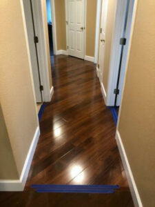 A hallway featuring newly installed dark wood flooring with painter's tape, completed by Stormtroopers Home Improvement in Port St. Lucie, FL.