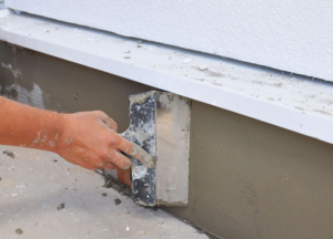 A handyman applying stucco to a building foundation with a trowel for Tito's Home Improvement LLC in Stamford, CT.