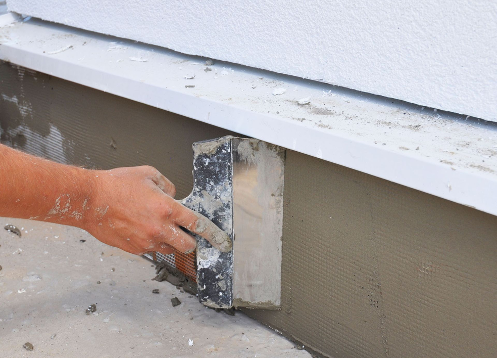 A handyman applying stucco to a building foundation with a trowel for Tito's Home Improvement LLC in Stamford, CT.