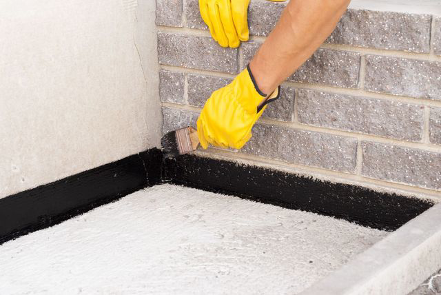 A handyman applying black waterproofing sealant to a concrete corner for Tito's Home Improvement LLC in Stamford, CT.