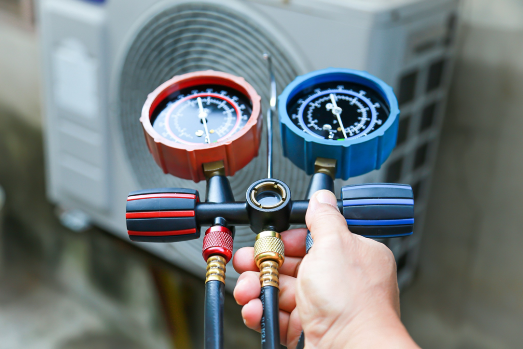 A hand holding HVAC manifold gauges to check an outdoor air conditioning unit for Advanced Mechanical Contractors, Inc. in Nashville, TN.