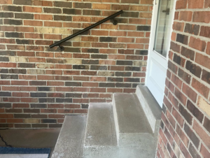A newly installed black metal handrail on a brick wall next to concrete steps by HC Homes & Consulting in Bowling Green, KY.