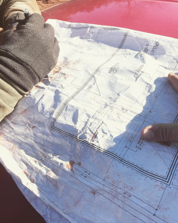 A person's gloved hands reviewing crumpled construction blueprints for a project by Bryan Lee Builds in Oklahoma City, OK.
