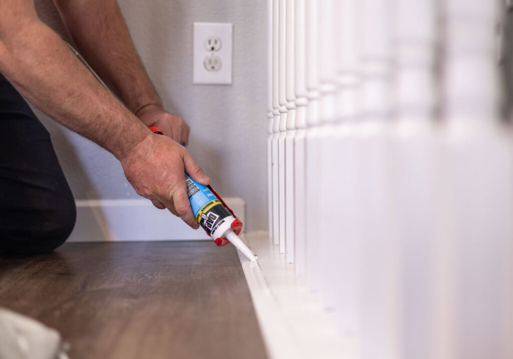 A handyman applying caulk along baseboards, a service provided by Ace Handyman ABQ SF in Albuquerque, NM