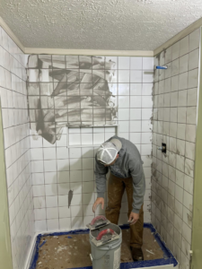 A handyman applying grout to white shower tiles during a bathroom renovation by Home Changes in Knoxville, TN