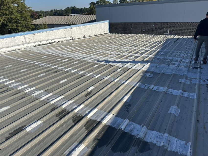 A handyman applying sealant to a commercial metal roof for Knight Construction Services in Brick, NJ.