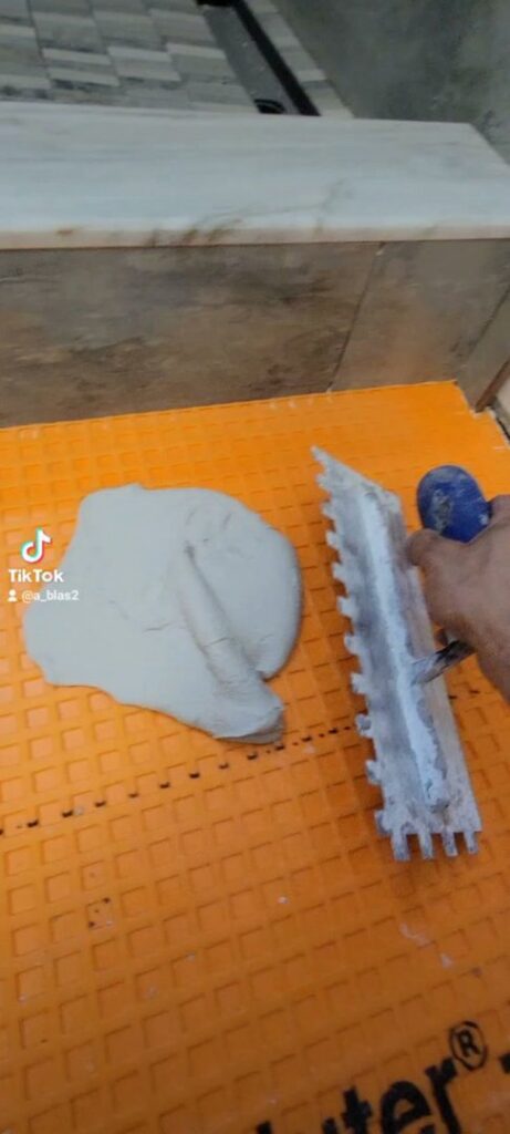 A handyman applying thin-set mortar to a Schluter Ditra waterproofing membrane, demonstrating tile preparation by Blas Home Remodeling LLC in New Castle, DE.