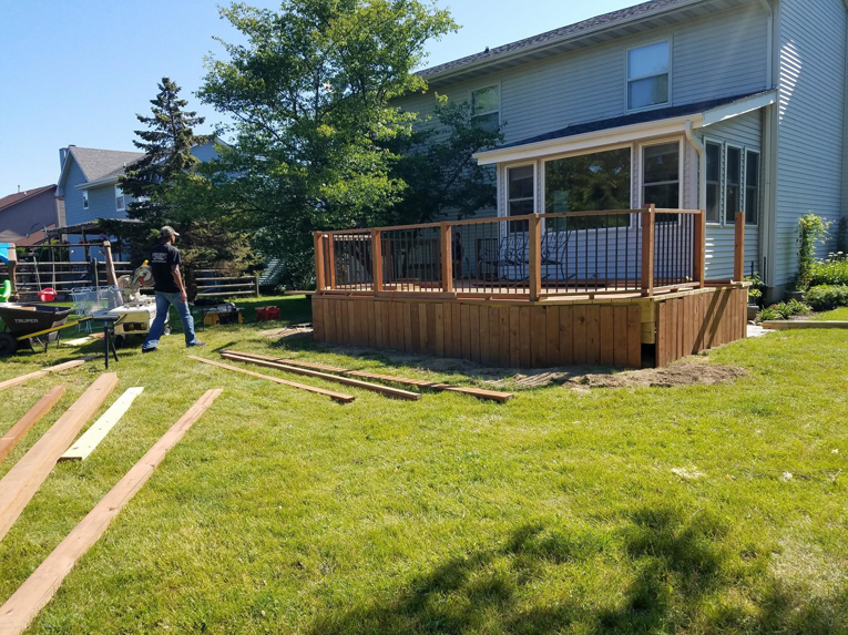 A handyman working on building a new wooden deck in a backyard for Screwheads Decking And Supply Store in Racine, WI