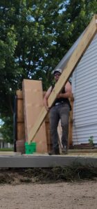 A handyman carrying a long wooden beam for a construction project by SAM'S Handywork LLC in Independence, IA.