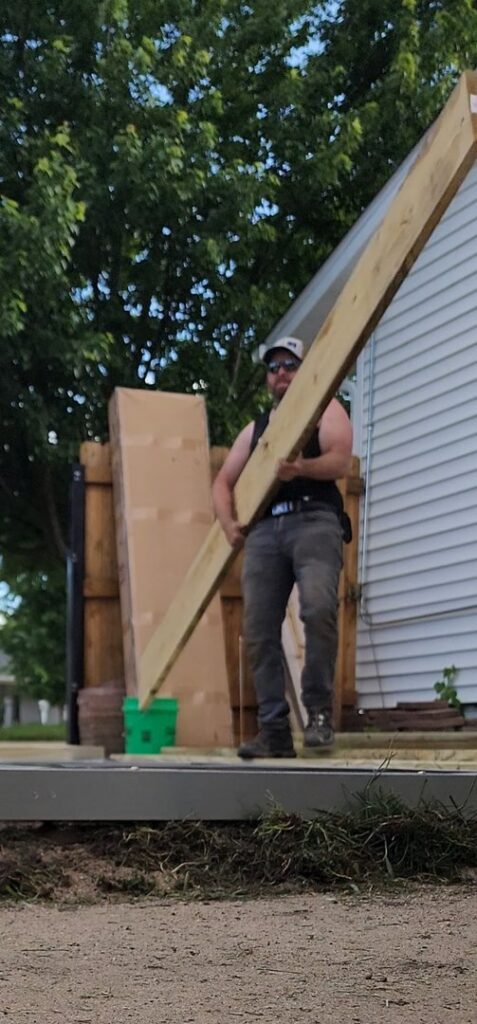 A handyman carrying a long wooden beam for a construction project by SAM'S Handywork LLC in Independence, IA.