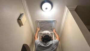 A handyman changing an air filter in a ceiling vent, a common maintenance task by AC Services of Minden in Minden, LA.