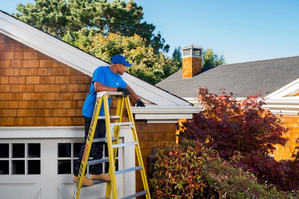 A Handyman Connection of Wichita East professional cleans gutters from a ladder in Wichita, KS.